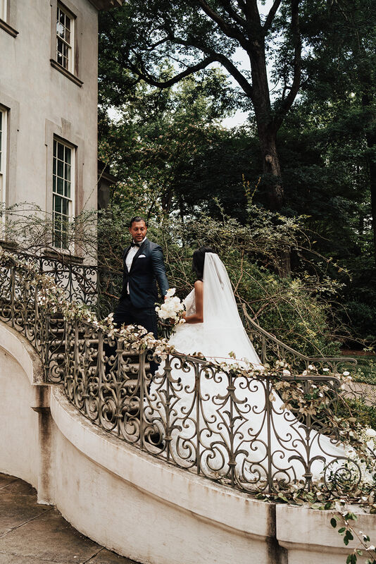 Groom leads bride up steps with beautiful swirly railing covered in greenery to their Scottsdale resort wedding venue