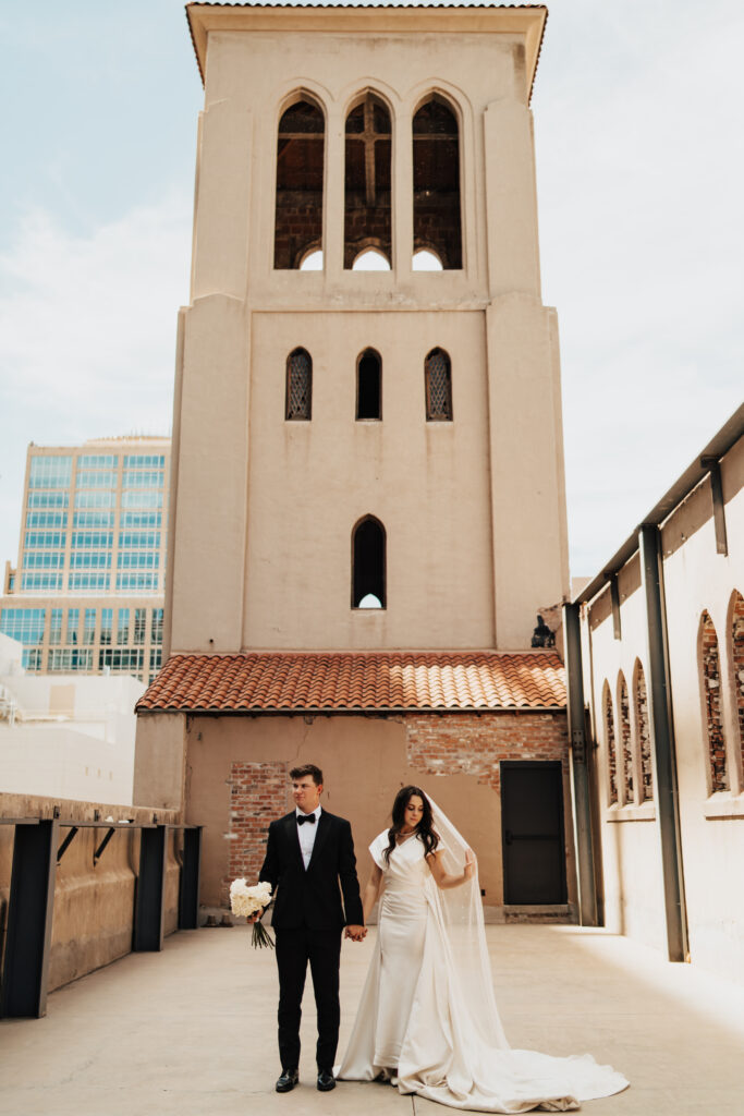 Bride and groom hold hands in front of what used to be a bell tower before the 1984 fire at The Abbey on Monroe