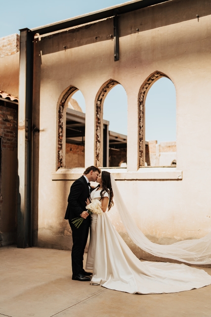 Bride and groom kiss outside the Abbey on Monroe wedding venue with lancet arch windows behind them